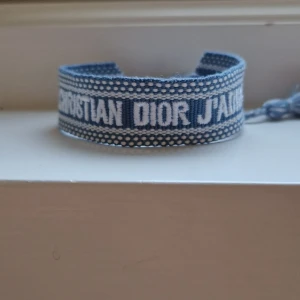 Christian Dior J'Adior armband Blå - Snyggt armband från Christian Dior med texten 'J'Adior' broderad i vitt. Armbandet har en vävd design med vita detaljer och avslutas med två coola tofsar i blått och vitt. Perfekt accessoar för att lyfta din outfit med lite lyxig vibe. Justerbar storlek (Passar alla) ✌️ Hör av dig vid minsta fråga!