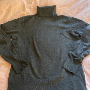 Mörkgrå polotröja i mjuk ullmix - Mörkgrå polotröja med ribbad hög krage och muddar. Tröjan är stickad i en mjuk ullmix och har lång ärm. Perfekt för lager-på-lager och chill höst- och vinterstil.