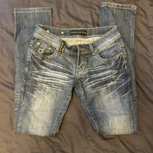 Blå jeans från Musketeer Denim med dragkedjor - Snygga blå jeans från Musketeer Denim med slitningar framtill och coola gula dragkedjor på bakfickorna. Jeansen har klassisk femficksdesign, kontrastsömmar och en rak passform. Perfekta för dig som vill sticka ut med detaljer och streetkänsla. Tyvärr för små för mig 💔