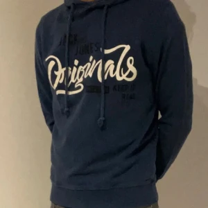Blå hoodie från Jack & Jones - Säljer en marinblå hoodie från Jack & Jones med vit och svart tryckt text 'Originals' på bröstet. Tröjan har huva med snörning och långa ärmar. Perfekt för dig som gillar en avslappnad och stilren look. Limited edition. Riktigt bra pris på 450!! S/M