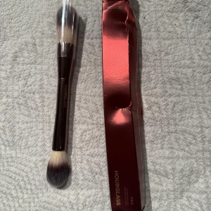 Hourglass Veil dubbelsidig sminkborste - Lyxig dubbelsidig sminkborste från Hourglass, modell Veil. Ena sidan har en fluffig, rundad borste och andra sidan en plattare, vinklad borste. Borsten är i syntetiskt material med svart och vit ombre-effekt. Perfekt för foundation, puder eller highlighter. 