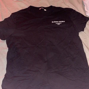 Svart t-shirt från Björn Borg XXL - Svart t-shirt från Björn Borg i storlek XXL med vit logotyp och text 'Stockholm 1984' på bröstet. Klassisk rund hals och korta ärmar. Mjuk och skön bomullskvalitet som passar perfekt till jeans eller shorts.