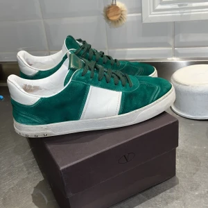 Valentino Garavani gröna sneakers mocka - Snygga gröna och vita sneakers från Valentino Garavani i mocka och skinn. Klassisk låg modell med gröna skosnören, vita detaljer och små nitar på sulan. Perfekta för dig som vill sticka ut med exklusiva och trendiga skor. Riktigt fräscha dojor skick 7,5/10. 4 nitar borta se bild (4) även box och påsar följer självklart med. Priset kan gå ner vid snabbt intresse.