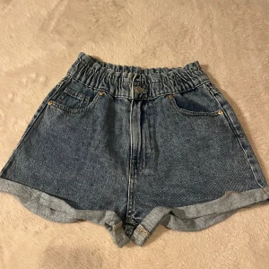 Blå denimshorts  - Snygga blå denimshorts från FB Sister köpta på new yorker med hög midja och resår i midjan. Klassisk femficksmodell med uppvikta benslut och knappstängning framtill. Perfekta för varma dagar och enkel att matcha med allt.