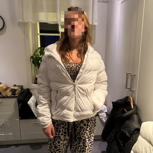 Vit pufferjacka med huva - Säljer en snygg vit pufferjacka med huva och dragkedja framtill. Jackan har quiltad design och två fickor med dragkedja. Perfekt för kalla dagar när du vill hålla dig varm och ändå se fräsch ut.