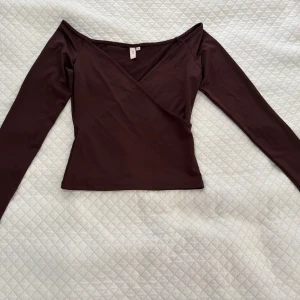 Brun topp lång ärm från Nelly - Säljer en mörkbrun omlottopp från nelly i storlek xs med lång ärm och v-ringad hals. Toppen har en slim passform.