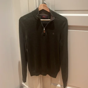 Mörkgrön merinoulltröja Morris S - Snygg mörkgrön långärmad tröja från Morris i 100% merinoull. Tröjan har en stilren half zip-dragkedja vid halsen och diskret broderad logga på bröstet. Perfekt för dig som gillar klassisk och clean stil med lite edge. Skick 10/10