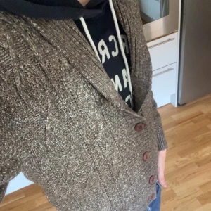 Brun stickad kofta från River Island - Säljer en brunmelerad stickad kofta från River Island i storlek M. Koftan har snyggt kabelstickat mönster, ribbade muddar och fem bruna knappar framtill. Perfekt för lager-på-lager och chill stil under höst och vinter.