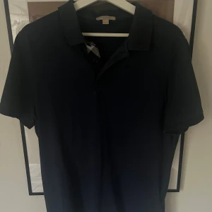 Burberry Piké - Klassisk mörkblå pikétröja från Burberry med korta ärmar och krage. Storlek L men sitter som en M.