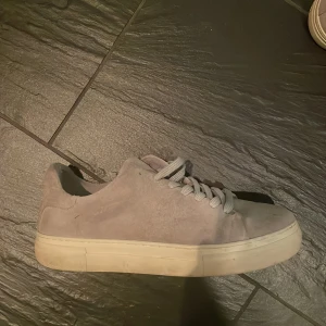 Grå selected homme skor  - Säljer ett par stilrena sneakers i ljusgrå mocka med platt vit sula och rund tå. Skorna har klassisk snörning och en enkel, minimalistisk design som passar till det mesta. Perfekta för dig som gillar en clean look och mjuka material. ‼️Har den defekt syns på sista bilden nypris 1199‼️