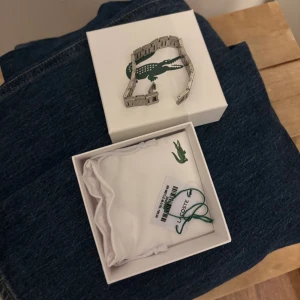Silverfärgat armband från Lacoste - Stilrent armband i silverfärgad metall från Lacoste med klassisk krokodil-logga på länkarna. Kommer i original ask och tygpåse med logga. Perfekt accessoar för dig som gillar en clean och sportig look. Helt oanvänt.