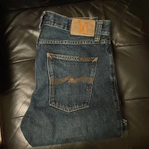 Mörkblå Nudie Jeans Straight Fit - Snygga mörkblå jeans från Nudie Jeans med klassisk femficksdesign och gul kontrastsöm på bakfickorna. Modellen har rak passform och normal midja, tillverkade i slitstarkt bomullsjeansmaterial. Perfekta för dig som gillar tidlös stil och bra kvalitet.