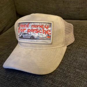 Need money for Porsche keps - Snygg grå keps från Revenite med mesh på sidorna och baksidan. Framtill finns ett stort patch med texten 'need money for Porsche' och en bild på en Porsche. Kepsen har böjd skärm och justerbar passform. En allmänt skön velvet keps som passar till allt och sticker ut. Använd Max 3 gånger så kepsen är i nyskick!!!