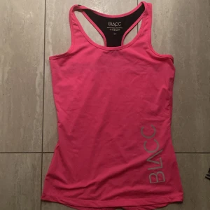 Rosa träningstopp från BLACC - Säljer en snygg rosa linnetopp från BLACC med brottarrygg och svart detalj på baksidan. Toppen är i stretchigt material, perfekt för träning. BLACC-logga i silver på framsidan. Materialet är 88% polyester och 12% elastan.