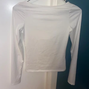Vit långärmad topp med cut out H&M - Säljer en vit långärmad topp från H&M med snygg cut out-detalj framtill och twistad knut vid halsen. Toppen är figurnära och har en stilren look som passar perfekt till jeans eller kjol. Tillverkad i mjuk bomull för skön känsla hela dagen.