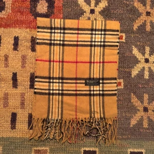 Vintage Burberry Halsduk - -Riktigt bra skick. Nypris på dessa ligger på runt 5000kr, vilket gör detta till ett sjukt bra pris! Halsduken är gjord i Lamull, och är perfekt inför hösten och den kommande vintern. Anledningen till att det står ”Burberry’s” och inte ”Burberry” på lappen är eftersom halsduken är från några år tillbaka, innan de bytte namn! Om du har någon fråga är det bara att skriva till mig. /elgnce (5)