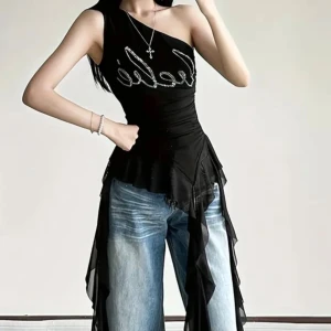 Svart oneshoulder topp från Leebé M - Säljer en svart oneshoulder topp från Leebé med glittrig logga framtill. Toppen har asymmetrisk design, croppad passform och långa volangdetaljer i mesh som hänger ner längs sidorna. Materialet är polyester och toppen är tight med coola detaljer som gör den unik.