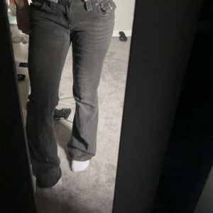 Svarta bootcut jeans med rå kant - Snygga svarta jeans med bootcut passform och rå, fransig kant nertill. Jeansen har klassisk femficksdesign och är tillverkade i ett robust denimtyg. Perfekta för dig som gillar en avslappnad men trendig stil.