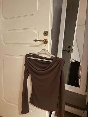 Brun topp - Säljer en brun långärmad off shoulder topp på ena armen . Toppen har en tight passform och är tillverkad i ett mjukt material som sitter skönt mot kroppen. Storlek xs ifrån Nelly, helt ny!