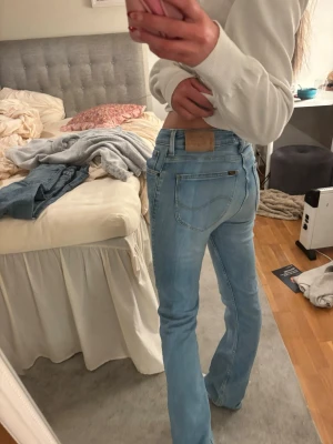 Ljusblå bootcut jeans från Lee - Säljer ett par ljusblå jeans med klassisk femficksdesign och bootcut-ben. Jeansen har normal passform och är tillverkade i mjukt denim-material. Medelhög midja Snygga detaljer med Replay-logga på bakfickan och metallknapp framtill. Perfekta för dig som gillar retrovibe och bekväma jeans. Pris kan diskuteras 
