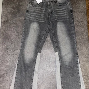 Grå flared jeans från Gallery Dept. - Grå jeans från Gallery Dept. med coolt tvättad look och ljusare paneler längs benen. Klassisk femficksmodell. Materialet är robust denim i bomull. Perfekt för dig som vill sticka ut med en edgy stil.