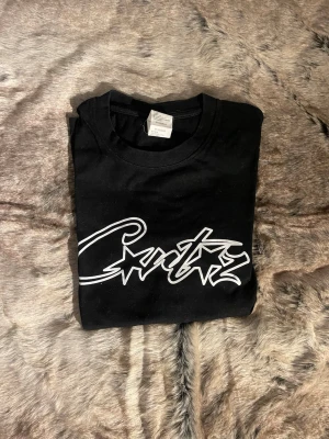 Svart t-shirt med vit logga - Svart t-shirt i bomull med vit grafisk logga framtill. Klassisk rund halsringning och korta ärmar. Enkel och clean design som passar till allt, med en streetig vibe och skön passform.