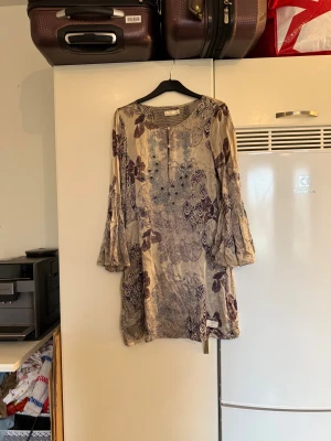 Odd molly tunika  - Säljer en supersnygg silkes tunika i en grå/ beige färg. Den har fina pärlor på framsidan av tunika. Tunikan har ett fint mönster o färgerna lila och brunt. Från märket Odd Molly. Storlek 2 som enligt deras storleksguide motsvarar en M. Mycket fint skick, jag hittar inga synliga anmärkningar eller defekter.  