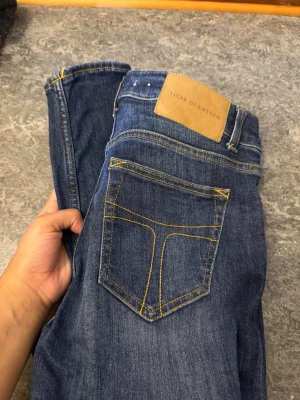 Blå jeans från Tiger of Sweden 29/32 - Snygga blå jeans från Tiger of Sweden med klassisk femficksdesign och kontrastsömmar i gult. Modellen heter Slight och har en rak passform. Jeansen är tillverkade i jeansmaterial och har en läderpatch med logga bak i midjan.