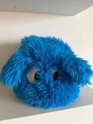 Blå fluffig pälsmössa med stora ögon - Unik och lekfull blå pälsmössa med superfluffigt syntetmaterial och stora, runda ögon framtill. Västen har en rund form och sticker verkligen ut med sin färgstarka look. Perfekt för dig som vill ha något riktigt annorlunda och roligt i garderoben!