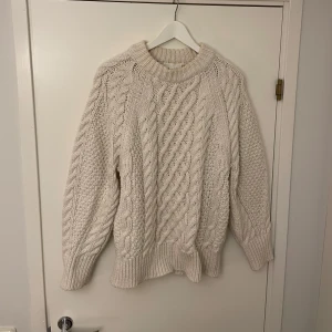 Oversized Beige stickad tröja med kabelmönster - Säljer en chunky beige stickad tröja med grovt kabelmönster och bred ribbad kant vid hals, ärmslut och nederkant. Tröjan har långärmade och loose passform, perfekt för kyliga dagar. Materialet är mjukt och tjockt, vilket gör den extra mysig.
