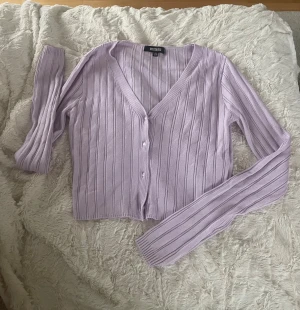 Liliac ribbad tröja från Missguided - Säljer en ljuslila kofta från Missguided i storlek 36. Koftan är ribbstickad med v-ringning och har långa ärmar samt knappar framtill. Materialet är mjukt och stickat, perfekt för lager på lager under vår och höst.