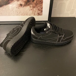 Nike Jordan 1 Low svart  - Säljer ett par Nike Jordan 1 Low sneakers i svart med kontrasterande vita sömmar och klassisk swoosh på sidan. Skorna har snörning, rund tå och platt sula. Materialet är en mix av mocka och syntet, med detaljer i vitt och lite rött på tungan. De är ett par Travi scott Phantom. Säljer för dom är för småa.