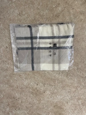 Rutig beige väst i ullmix - Säljer en snygg väst med rutigt mönster i beige, grått och vitt. Västen har klassiska breda rutor och är tillverkad i en mjuk ullmix som känns både stilren och bekväm. Perfekt för dig som gillar en clean och tidlös look.