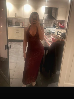 Vinröd glittrig långklänning - Supersnygg vinröd långklänning från Bubbleroom med glittrigt tyg och djup v-ringning. Klänningen är ärmlös med halterneck och har öppen rygg. Perfekt för dig som vill sticka ut med en glamorös look. Passformen är tight och markerar midjan. Har två likadana i storlek S och XS så skriv vilken ni vill ha 