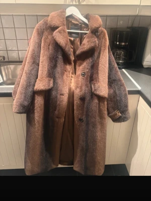 Brun pälsjacka från Rockandblue - Säljer en brun pälsjacka från Rockandblue i storlek 34. Jackan har bred krage, stora fickor och knäpps med knappar framtill. Materialet är mjukt och fluffigt med en lyxig känsla, perfekt för kalla dagar. Färgen är en mix av brun och mörkare toner.