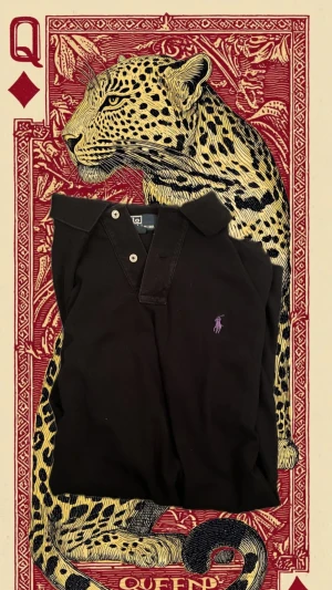 Svart piké från Polo Ralph Lauren - Svart pikétröja från Polo Ralph Lauren i storlek M. Klassisk krage, två knappar framtill och lila broderad logga på bröstet. Kortärmad och tillverkad i mjuk bomull som är skön mot huden. Perfekt för en clean och stilren look.