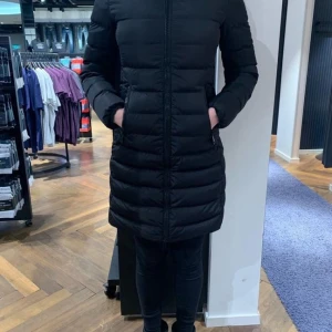 Svart lång pufferjacka från Moncler - Säljer en svart lång pufferjacka från Moncler med quiltade detaljer och dragkedja framtill. Jackan har huva, långa ärmar och snygga skinnpaneler på axlarna. Moncler-logga på ärmen. Perfekt för kalla dagar och riktigt stilren look.