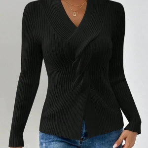 Svart ribbad långärmad Omlott tröja - Snygg svart ribbad omlott tröja med lång ärm och v-ringad hals. Tröjan har en unik omlott-detalj framtill och är tillverkad i ett stretchigt stickat material som sitter bekvämt. Perfekt att matcha med jeans för en cool och stilren look.