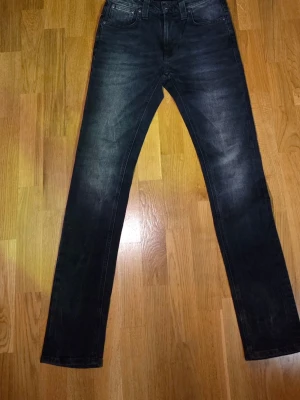 Mörkblå jeans från Nudie Jeans Co - Snygga mörkblå jeans från Nudie Jeans Co med klassisk femficksdesign och raka ben. Jeansen har subtila slitningar och kontrastsömmar, samt knappstängning fram. Perfekta för dig som gillar stilrena och tidlösa jeans med bra passform.