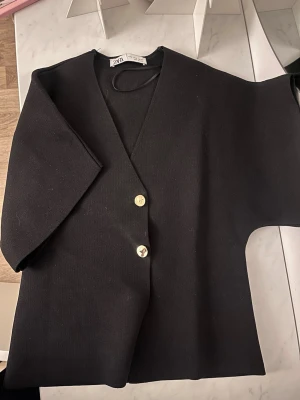 Svart bolerotopp från Zara med knappar - Svart topp från Zara med v-ringning och två snygga guldfärgade knappar framtill. Använd fåtal gånger! Vid intresse kan fler bilder skickas!