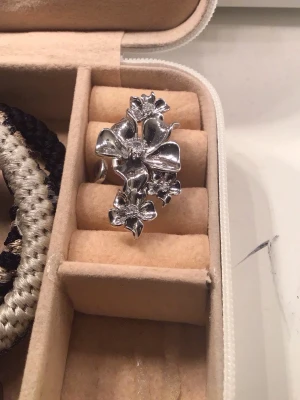 Ioaku la fleur ring i silver  - Säljer en stor och iögonfallande ring i silverfärg med detaljerade blommor som sträcker sig över fingret. Ringen har en glansig finish och flera blommor i olika storlekar, vilket ger en cool och unik look. Köptes för 600kr men säljer för 200kr❤️den är justerbar