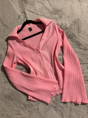 Rosa blus med vida ärmar  - Super snygg blus. Blusen har långärmade, utsvängda ärmar och tre knappar framtill. Materialet är lätt och har en snygg, skrynklig struktur som ger en cool vibe. Perfekt för dig som gillar färg och unika detaljer. Aldrig använd 