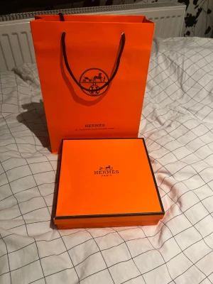  svart läderbälte med silver H-spänne - Exklusiv svart väst från i äkta läder med ett stort H-spänne i silverfärgad metall. Bältet har vita kontrastsömmar och levereras med originalförpackning, dustbag och certifikat. Perfekt för dig som gillar lyxiga detaljer och stilren design.