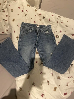 Bootcut jeans från Gina Tricot, blå - Snygga blå bootcut jeans från Gina Tricot i storlek 158. Jeansen har slitna detaljer på benen, klassisk femficksdesign och dragkedja med knapp framtill. Materialet är jeans med en cool tvättad look och kontrastsömmar.