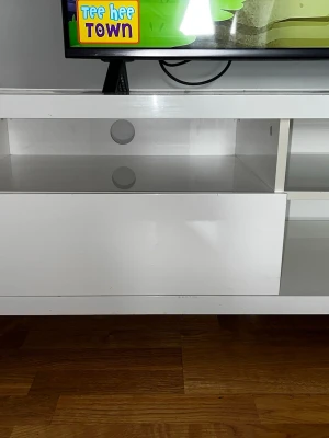 Tv bänk  - Bilderna visar en vit TV-bänk med öppna hyllor och lådor, väldigt fin tv bänk vill sälja snarast som möjligt men tv bänken får man jämta själv 