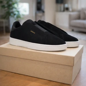 Svarta sneakers från Axel Arigato - Snygga svarta sneakers från Axel Arigato med minimalistisk design och vit platt sula. Skorna är tillverkade i mocka och har diskret guldfärgad logga på sidan. Perfekta för dig som gillar stilrena och moderna skor.
