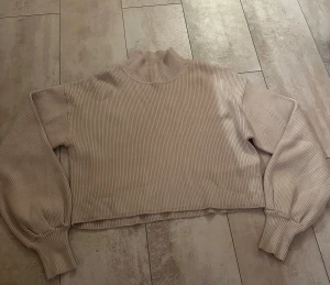Beige ribbad stickad tröja Gina Tricot - Säljer en beige stickad tröja från Gina Tricot i storlek L. Tröjan har ribbad struktur, hög hals och långa ärmar med breda muddar. Modellen är croppad och har en loose passform som ger en chill vibe. Perfekt att matcha med jeans eller kjol.