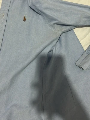 Ljusblå skjorta från Polo Ralph Lauren XS - Säljer en ljusblå skjorta från Polo Ralph Lauren i modellen Custom Fit. Skjortan har klassisk krage, knappar framtill och det ikoniska broderade logotypen på bröstet. Tillverkad i mjuk bomull och har långa ärmar. Perfekt för en clean och stilren look.