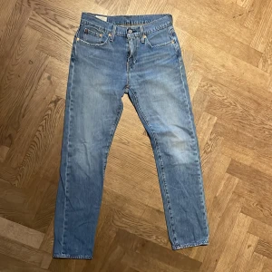 Levi's 501 ljusblå jeans - Säljer ett par klassiska Levi's 501 jeans i ljusblå tvätt. Modellen har raka ben, fem fickor och knappgylf. Jeansen är tillverkade i slitstarkt bomullsmaterial och har den ikoniska läderpatchen bak i midjan. Perfekt för dig som gillar tidlös denimstil.