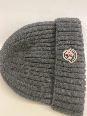 Grå ribbad Moncler mössa - Säljer en snygg grå mössa från Moncler med ribbad design och klassisk Moncler-logga framtill. Mössan är tillverkad i 100% bomull och har en bred uppvikt kant. Perfekt för dig som vill ha en stilren accessoar med exklusiv känsla. Fick denna mössa av en släkting men jag diggar inte mössor så vill sälja den. Hör av dig om du vill ha mer bilder eller om ni undrar över nåt fråga. Priset kan diskuteras. Billigare vid snabb affär😇